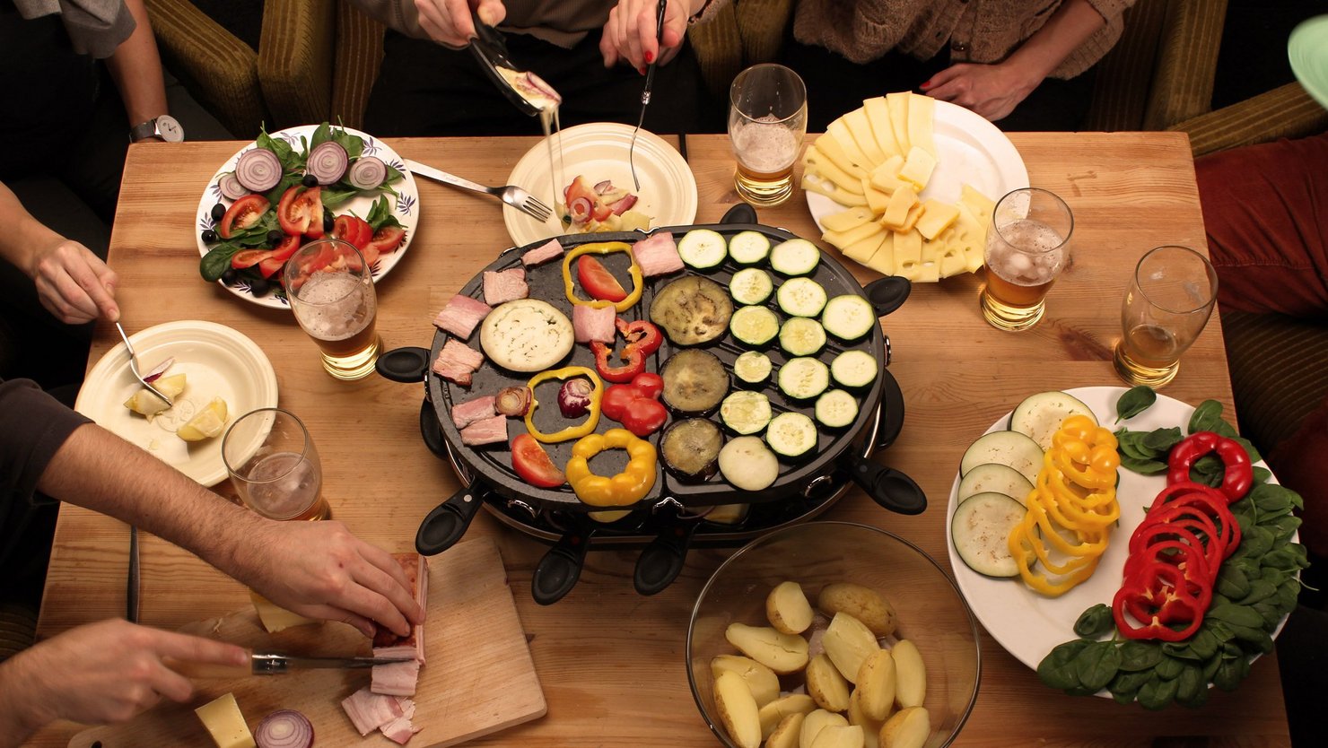 [Translate to PT (Portugal):] Table with raclette oven and dishes with potatoes, vegetables and cheese